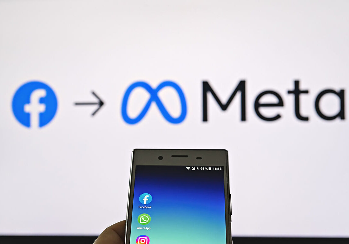 Smartphone display with logo of Facebook, WhatsApp and Instagram apps in hand against blurred META logotype on white monitor background: Tallinn, Estonia - October 29, 2021
