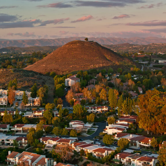 Aerial view of a hill in Thousand Oaks, California at sunset. There is a single tree a the top. Several apartment buildings are in the foreground, along with trees.